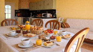 A breakfast table set with pastries, fruits, and beverages, surrounded by wooden chairs and a sofa in a bright room with kitchen cabinets in the background. - Pretty Provencal house in a quiet area 5 minutes walk from the sea in St Croix Martigues (Martigues)