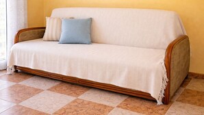 A sofa with a white cover and a blue pillow in a room with yellow walls and a tiled floor. - Pretty Provencal house in a quiet area 5 minutes walk from the sea in St Croix Martigues (Martigues)