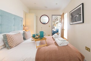 A hotel room with a bed, a bedside table with a kettle and pastries, a mirror, and a framed picture on the wall. - Scilly Stack (Penzance)