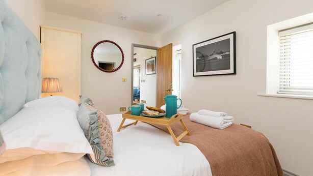 A bedroom with a bed, a bedside table with a tray of food, a mirror, a framed picture, and a window. - Scilly Stack (Penzance)
