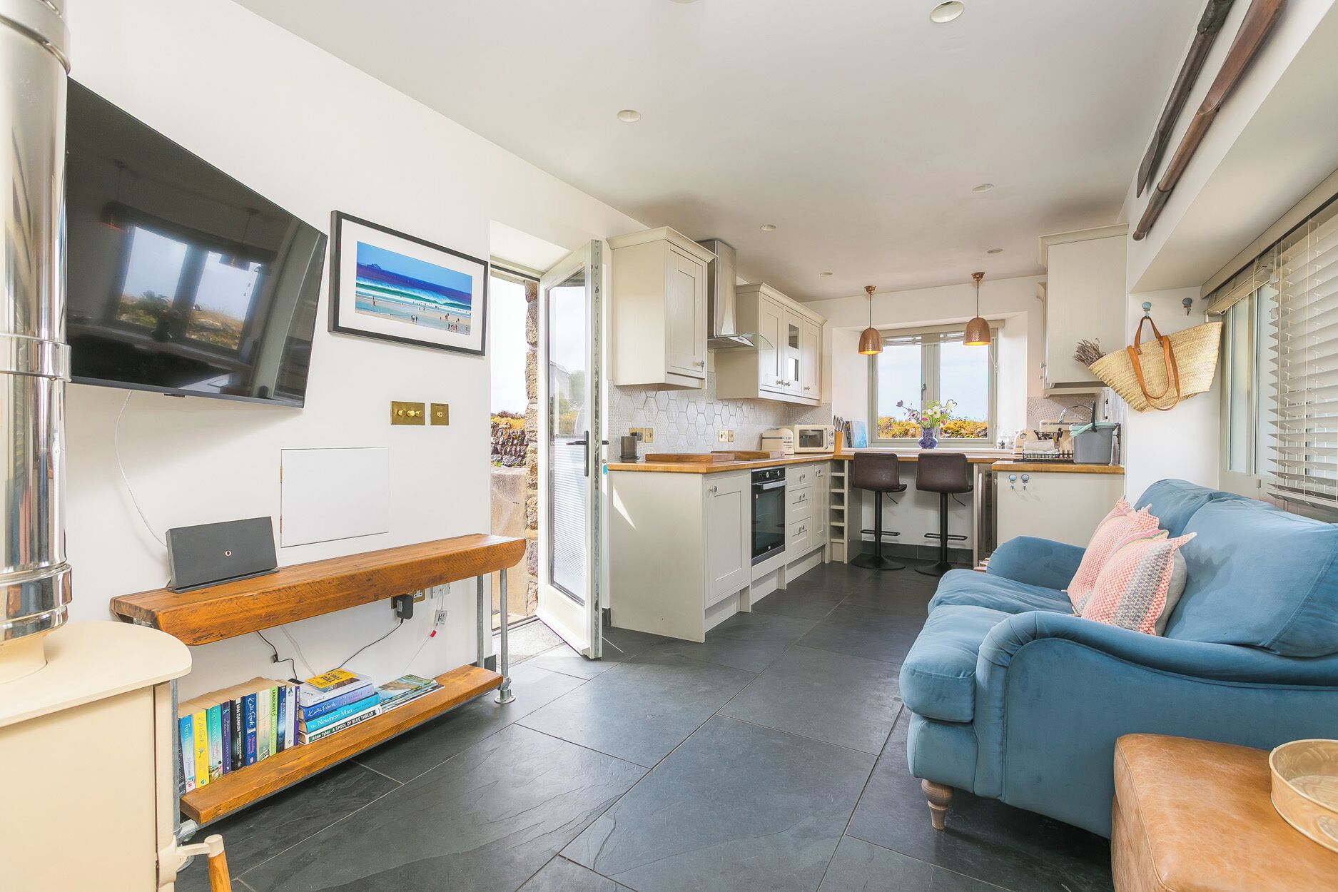 A compact kitchen with a dining area, a blue sofa, and a TV mounted on the wall.
