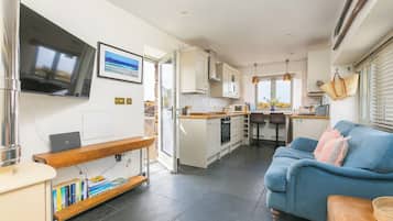 A compact kitchen with a dining area, a blue sofa, and a TV mounted on the wall.