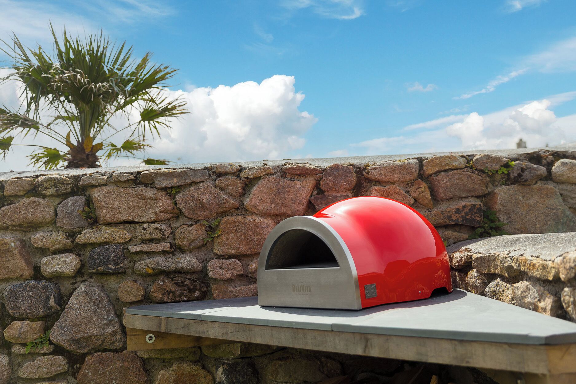 A stone wall with a red and silver outdoor oven on a wooden ledge.