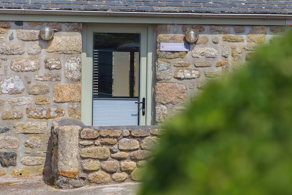 Un edificio de piedra con puerta metálica, una ventana pequeña y un letrero que dice 'SCILLY STACK'.
