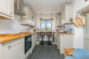 A compact kitchen with a view, featuring a stove, oven, microwave, and bar stools. - Scilly Stack (Penzance)