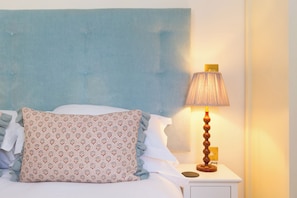 Una cama con un cojín estampado, un cabecero azul y una lámpara de noche en una mesita blanca.
