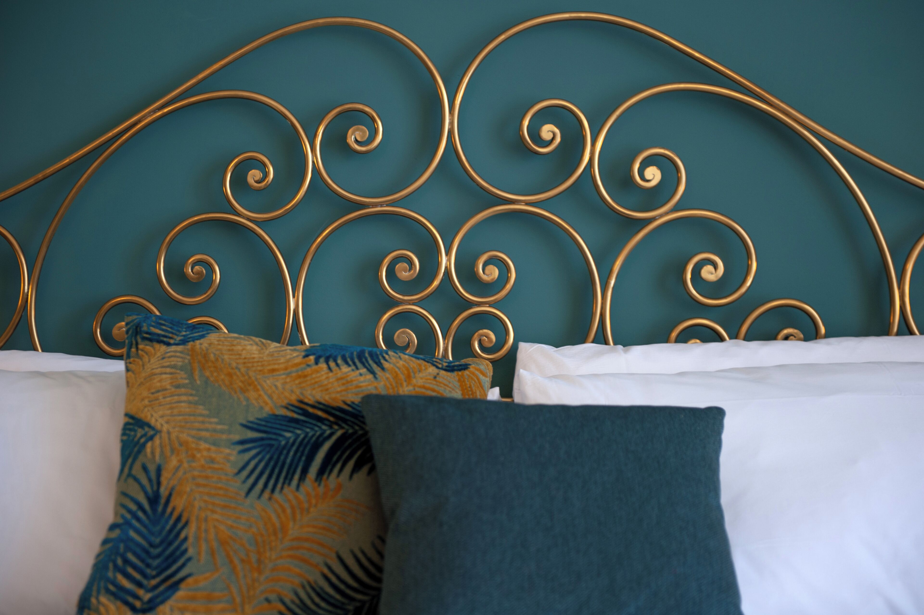A bed with a metal headboard, white and teal bedding, and patterned pillows.