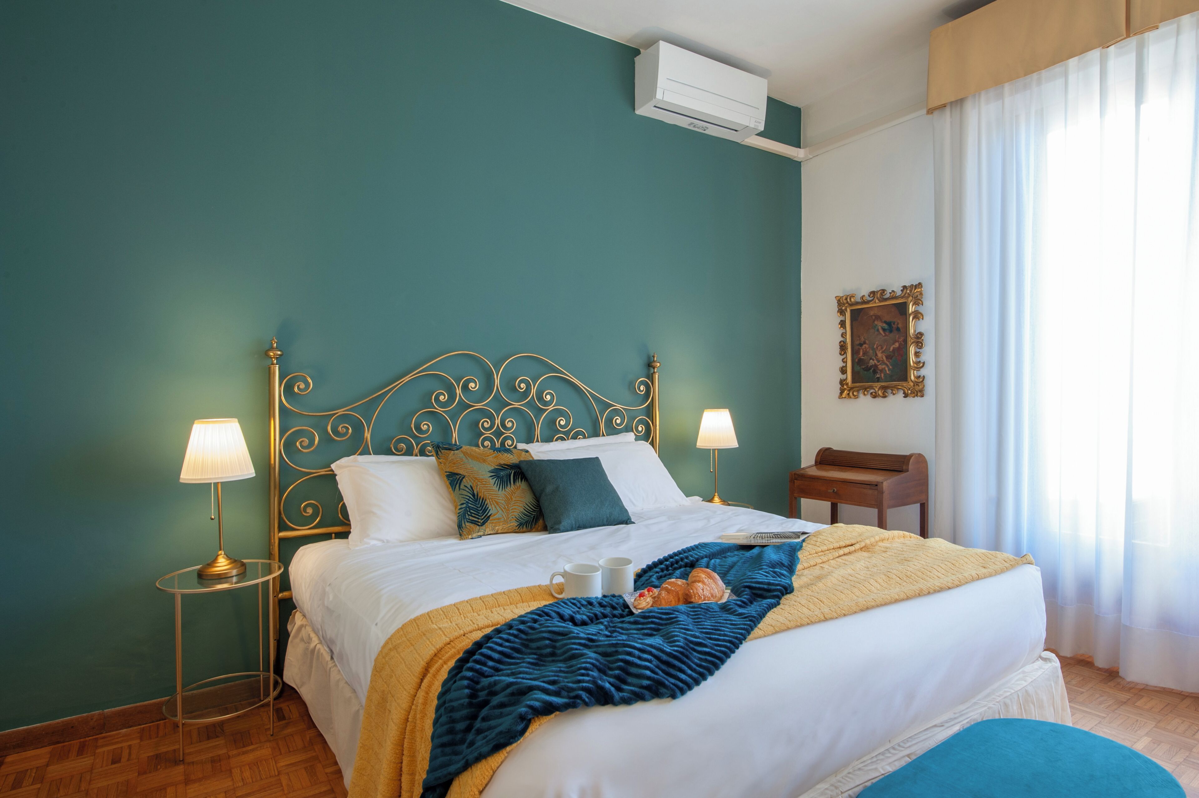 Una cama bien tendida con una manta azul, dos lámparas de noche y una mesita de madera.