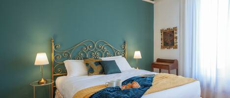 Una cama bien tendida con una manta azul, dos lámparas de noche y una mesita de madera.