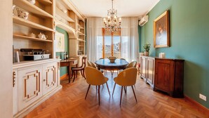 A dining area with a round table, chairs, a chandelier, and a view through the window. - Da Vinci - Flo Apartments (Florence)