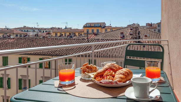 A balcony with a table set for breakfast, including croissants, a plate of pastries, and glasses of orange juice. - Da Vinci - Flo Apartments (Florence)