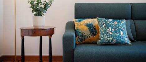 A room with a green sofa, a small round wooden table with a white vase and green plant, and a green floor lamp.