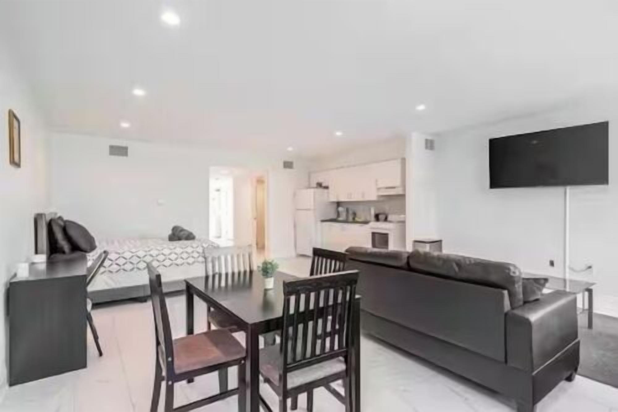 Una sala de estar moderna con sofá, mesa de comedor y sillas. Hay una zona de cocina con armarios y un televisor de pantalla plana montado en la pared.