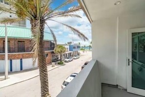 A balcony with a view of a street, a palm tree, and a building with a green roof. - The Purple Pelican~Beachfront w/ Ocean Balcony~#3 (Fort Lauderdale)