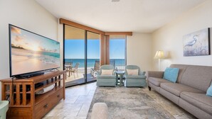 Olohuoneessa on televisio, sohva, kaksi nojatuolia, sohvapöytä ja suurista liukuovista avautuva näkymä merelle.