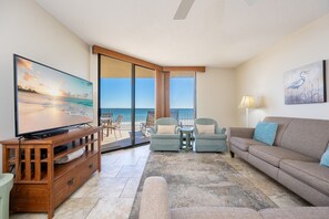 A living room with a television, a sofa, two armchairs, a coffee table, and a view of the ocean through large sliding glass doors. - Phoenix V 309 2 Bedroom Condo (Orange Beach)