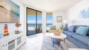 A spacious living room with a balcony, a sofa, a coffee table, and a TV. - Phoenix V 316 2 Bedroom Condo (Orange Beach)