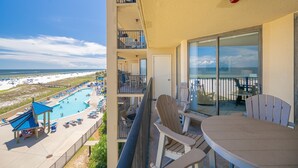 A balcony with a view of a pool and beach, a table with chairs, and a red fire extinguisher. - Phoenix V 316 2 Bedroom Condo (Orange Beach)