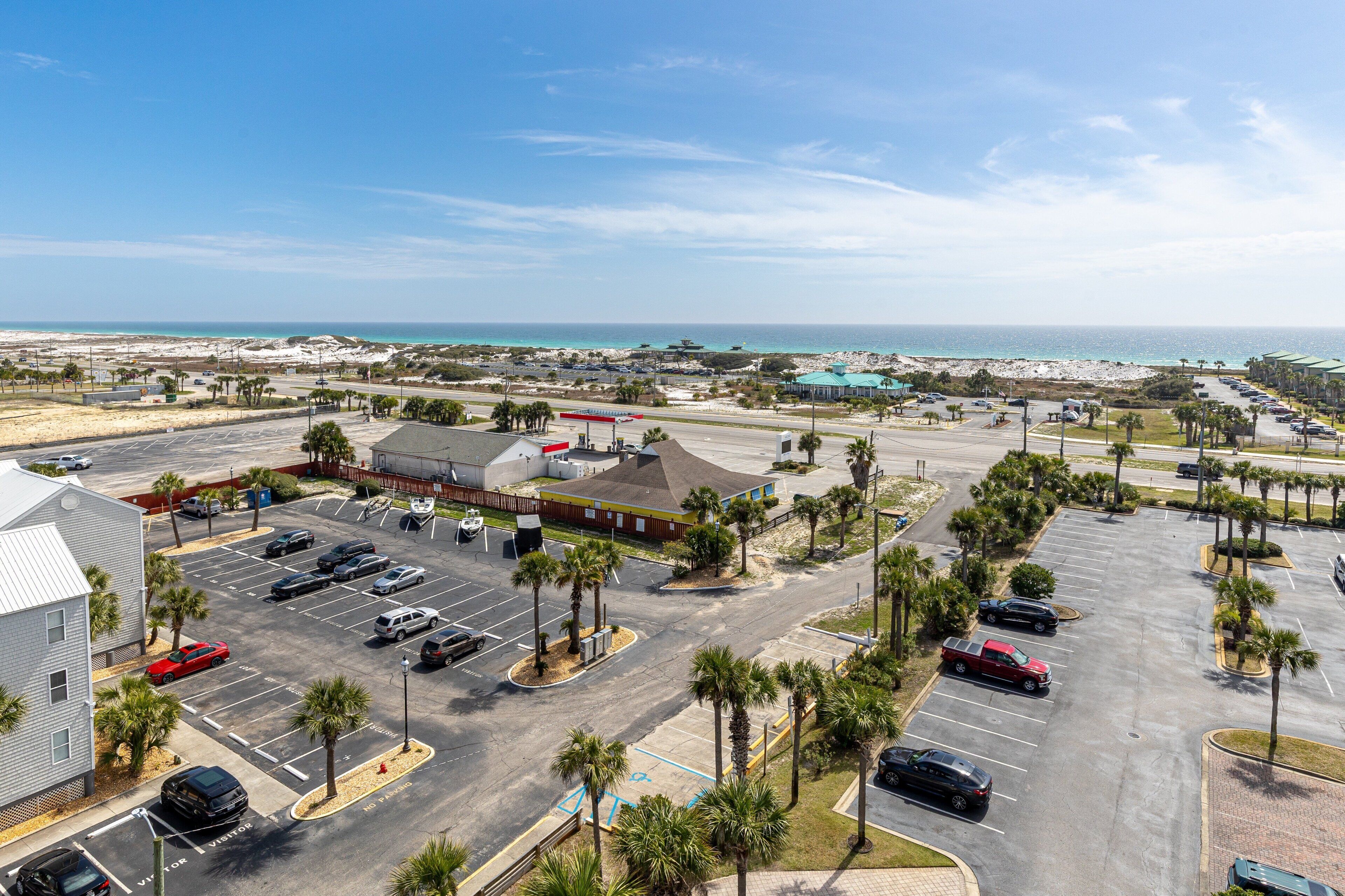 A parking lot with multiple cars, palm trees, and a building with a sloped roof.