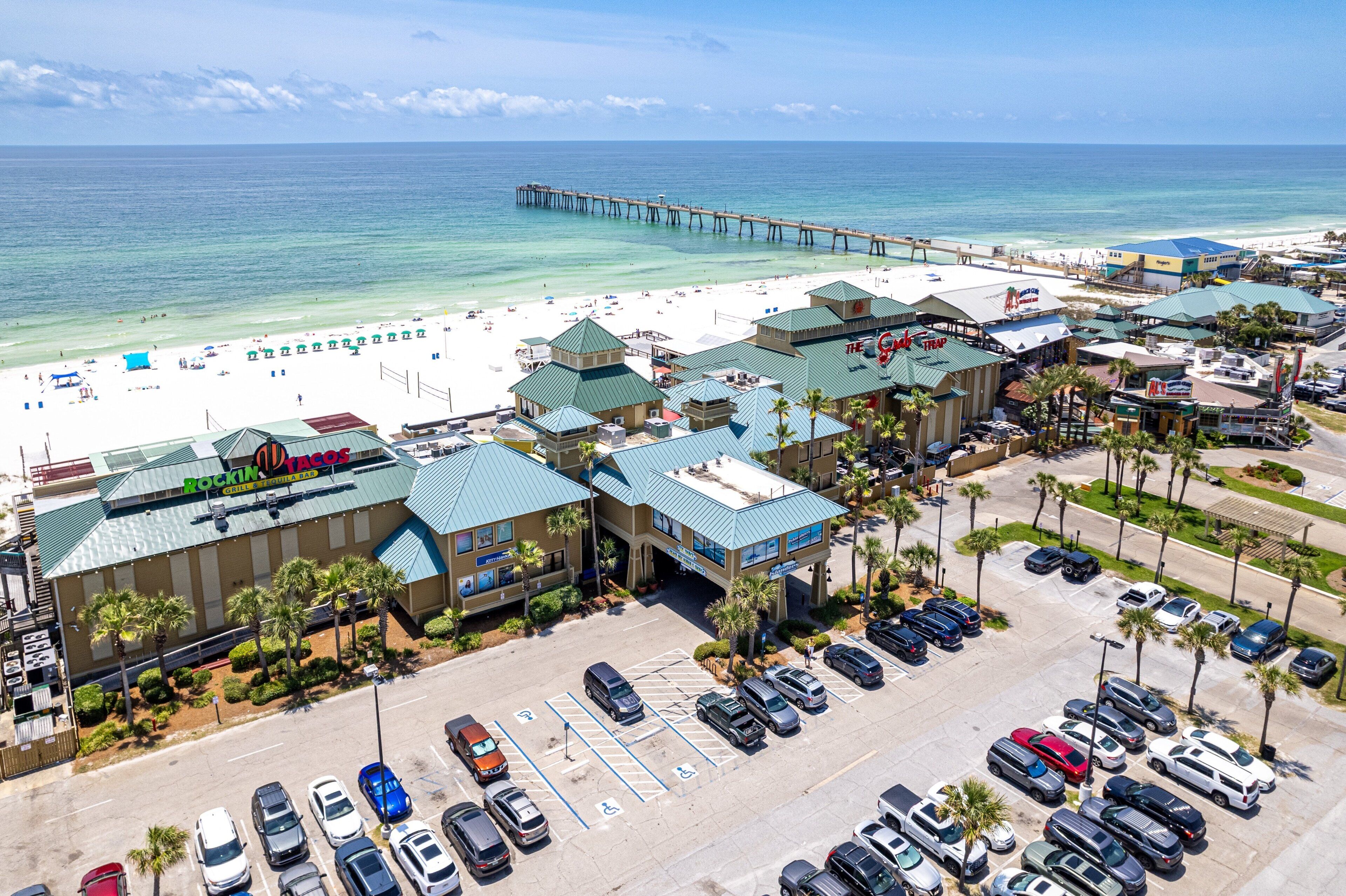 Ein Hotel am Strand mit Parkplatz, Zugang zum Strand und einem Pier im Hintergrund.