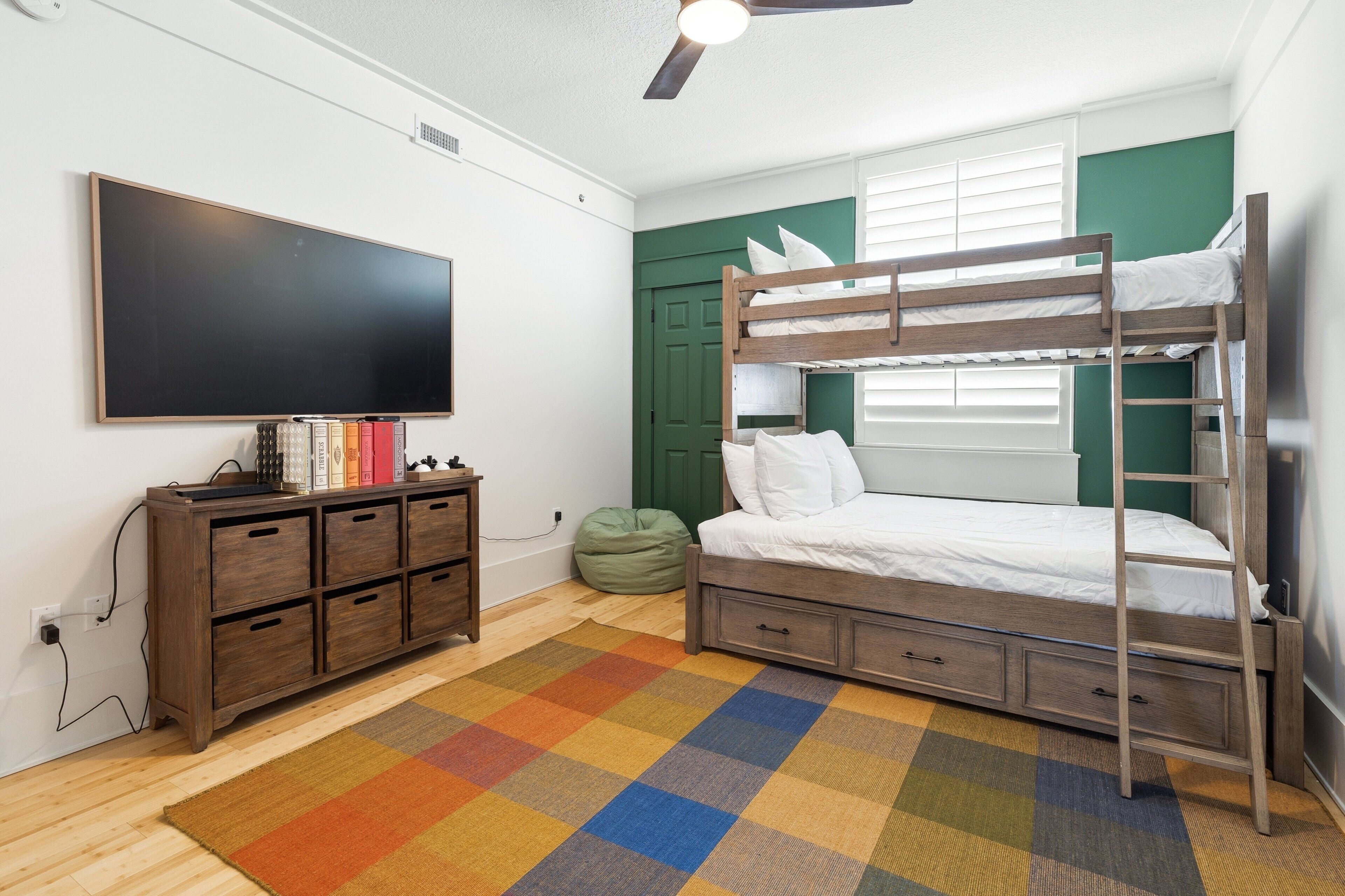 A bunk bed room with a television, wooden dresser, and a colorful rug.