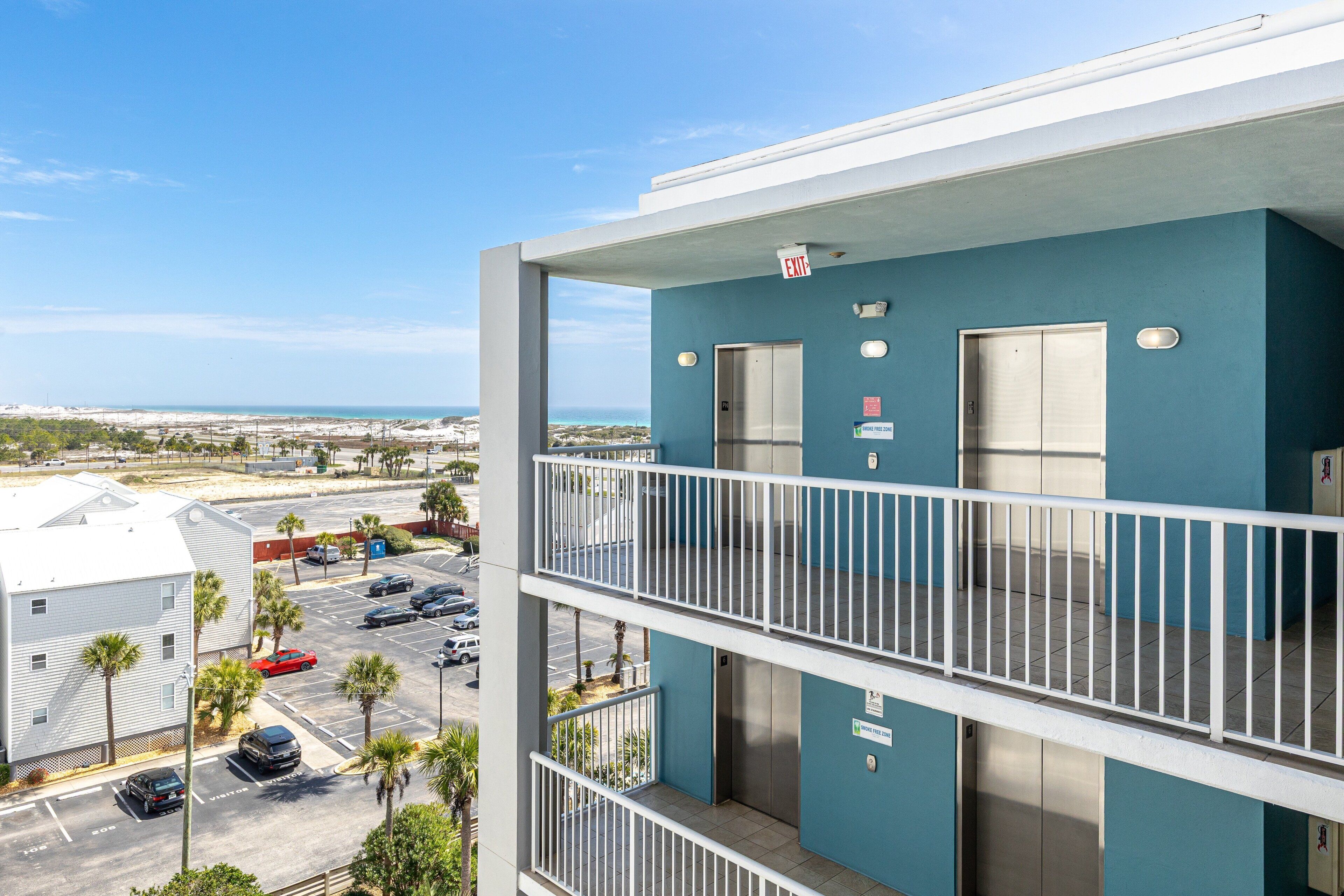 A multi-story building with a blue exterior, a balcony with a white railing, and an elevator.