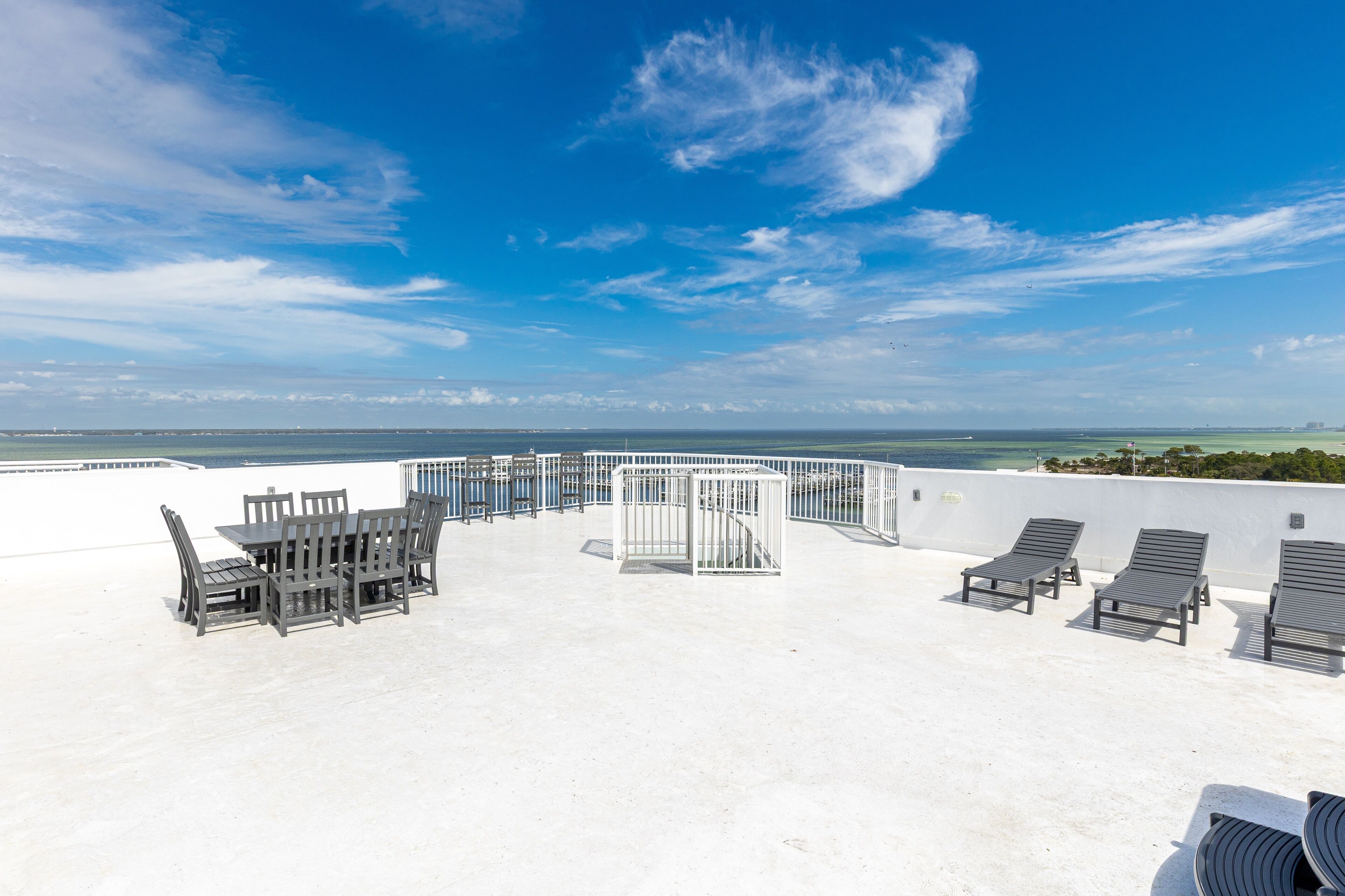 A rooftop terrace with a white floor, a table with chairs, and three lounge chairs.