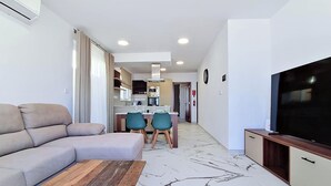 A modern living room with a sofa, a TV, and a dining area with chairs and a table. - Modern Penthouse Retreat with Rooftop City Views (Il-Mellieħa)