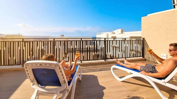 Two lounge chairs on a rooftop terrace with a view of buildings and the sky. - Modern Penthouse Retreat with Rooftop City Views (Il-Mellieħa)