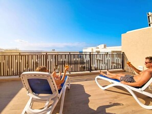 Dos sillones de relax en una terraza en la azotea con vistas a edificios y al cielo.