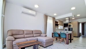 A modern living room with a sofa, a coffee table, and a dining area with chairs. - Modern Penthouse Retreat with Rooftop City Views (Il-Mellieħa)