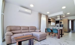 A modern living room with a sofa, a coffee table, and a dining area with chairs. - Modern Penthouse Retreat with Rooftop City Views (Il-Mellieħa)