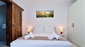 A bedroom with a bed, two bedside tables with lamps, a wooden wardrobe, a painting on the wall, and a towel on the bed. - Modern Penthouse Retreat with Rooftop City Views (Il-Mellieħa)
