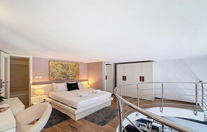 Ein modernes Hotelzimmer mit Bett, Nachttisch, Lampe und Blick auf den Balkon.