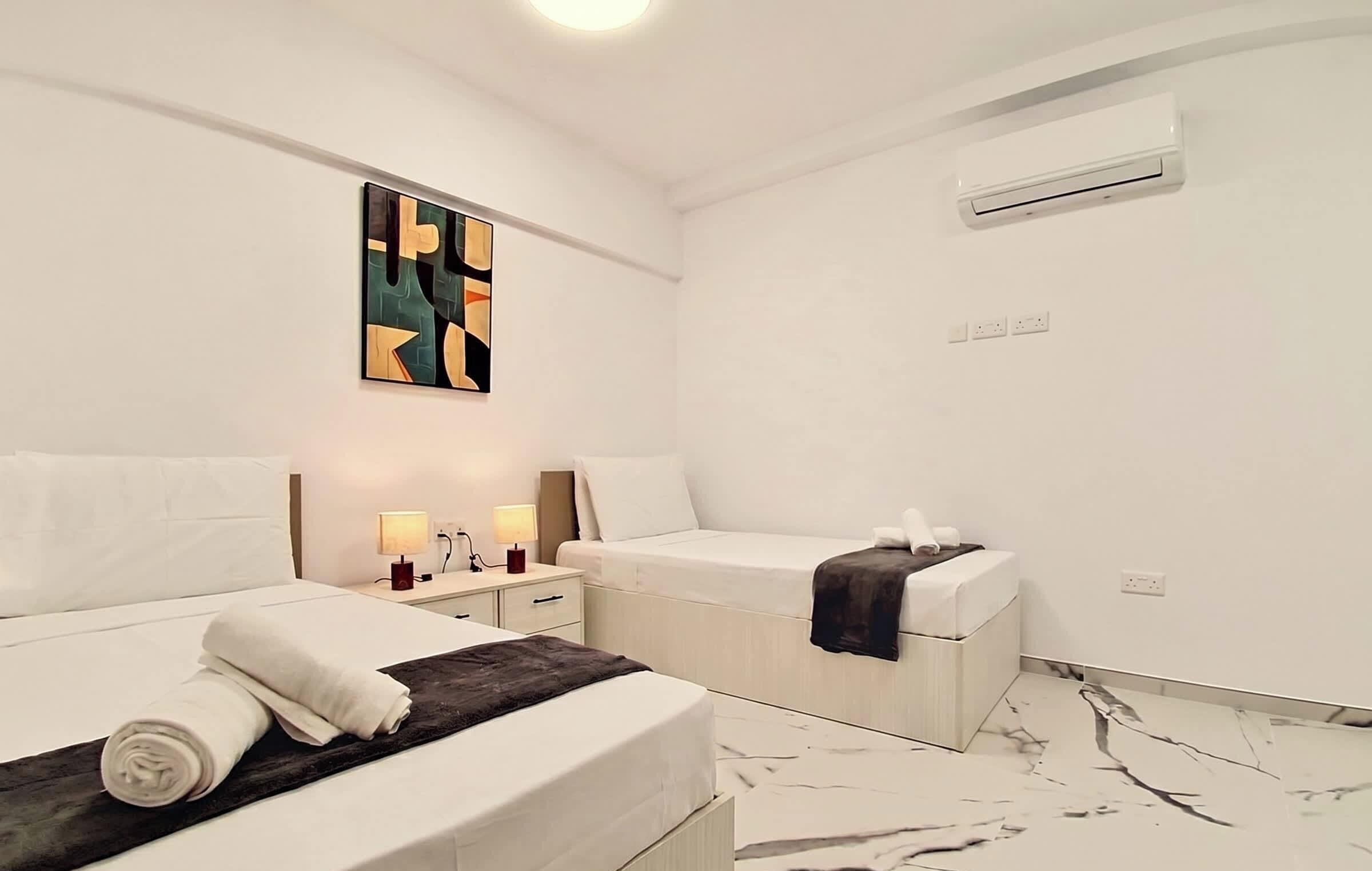 Habitación de hotel con dos camas, una mesita de noche con lámparas, aire acondicionado instalado en la pared y un suelo con estampado de mármol.