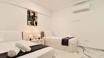 Habitación de hotel con dos camas, una mesita de noche con lámparas, aire acondicionado instalado en la pared y un suelo con estampado de mármol.