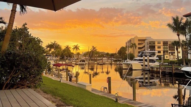 A marina with boats docked, a wooden deck, and a sunset in the background.