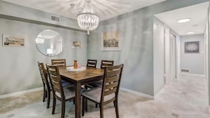 A dining room with a wooden table, six chairs, a chandelier, and framed artwork on the walls.