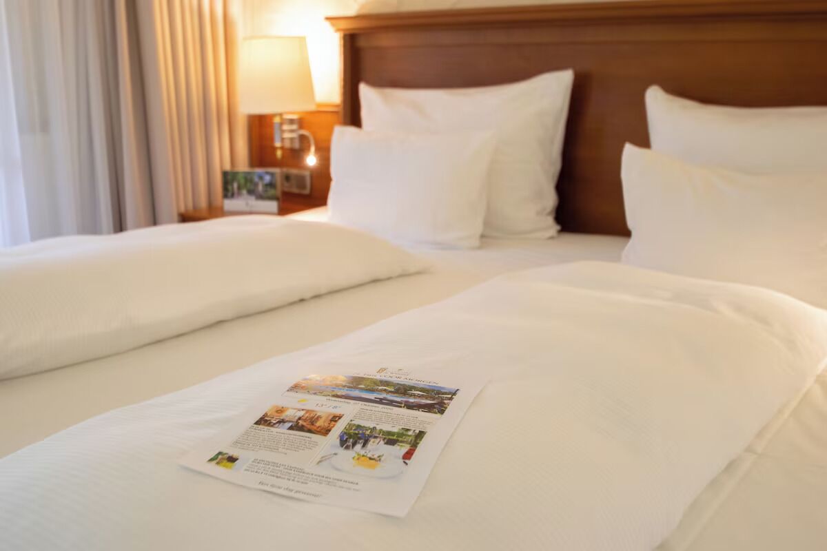 A hotel room with a neatly made bed, a nightstand with a lamp, and a brochure on the bed.