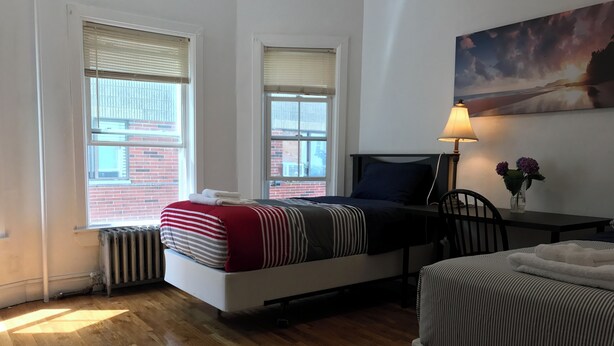 A bedroom with a bed, a chair, a table, a lamp, and a painting on the wall. - Spacious 4 bedroom apartment in adorable Boston with Central AC (Boston)
