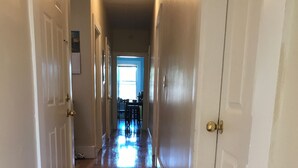 A hallway with wooden flooring, white walls, and doors leading to a dining area. - Spacious 4 bedroom apartment in adorable Boston with Central AC (Boston)