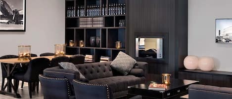Un área de estar moderna con un sofá de color oscuro, sillones a juego, una mesa de centro, una estantería con botellas y un cuadro en la pared.