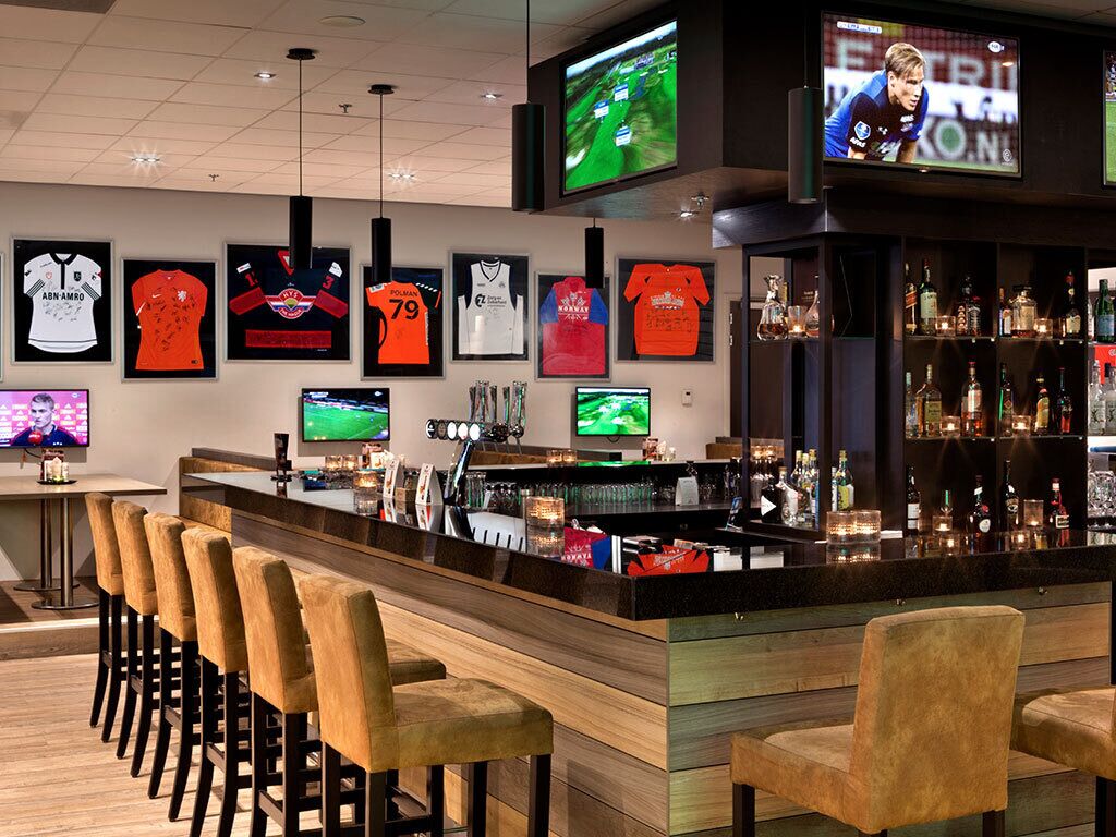 A bar area with a counter, bar stools, and framed jerseys on the wall.