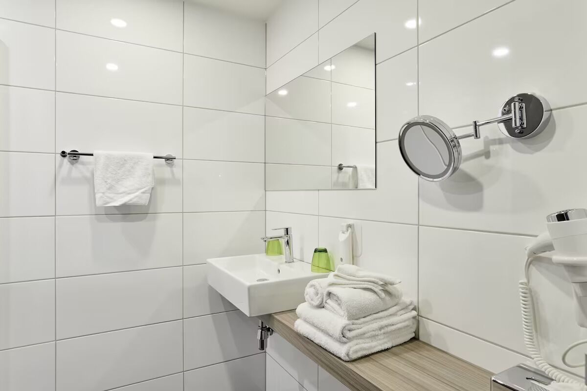 A modern bathroom with white tiles, a sink, a mirror, a towel rack, and a hairdryer.