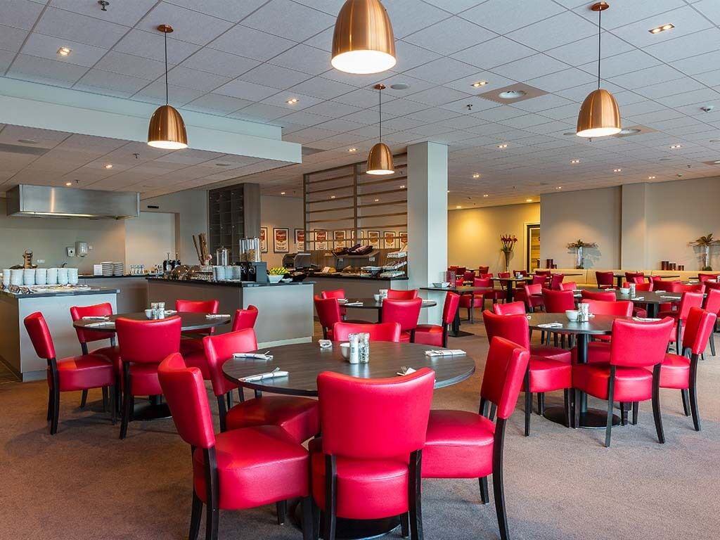 Een restaurant met rode stoelen en tafels, een bar en een keuken op de achtergrond.