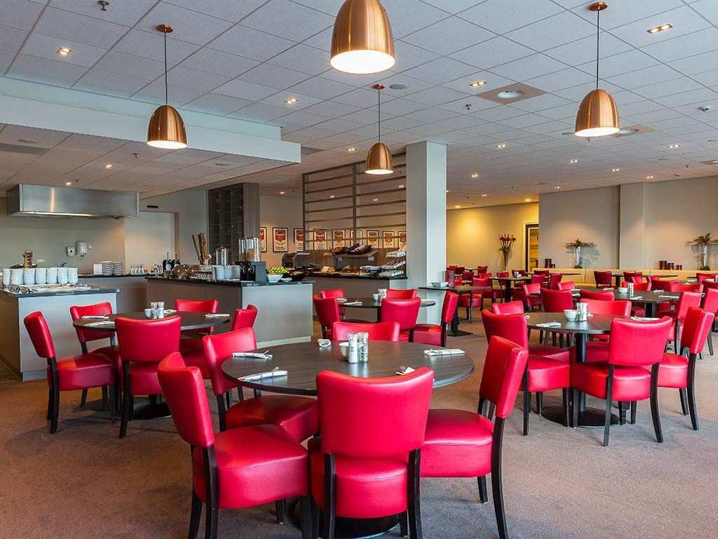 Ein Restaurant mit roten Stühlen und Tischen, einer Bar und einer Küche im Hintergrund.