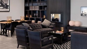 A modern lounge area with a dark-colored sofa, matching chairs, a coffee table, a bookshelf with bottles, and a framed picture on the wall.