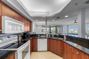 Une cuisine moderne équipée d’un four à micro-ondes, d’une cuisinière et d’un lave-vaisselle encastrés, de meubles de rangement en bois et d’une grande fenêtre donnant sur l’extérieur.