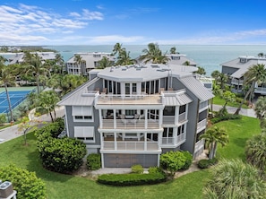 A multi-story building with balconies, a tennis court, and a view of the ocean.