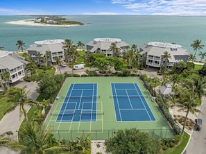 A tennis court surrounded by buildings with a view of the ocean.